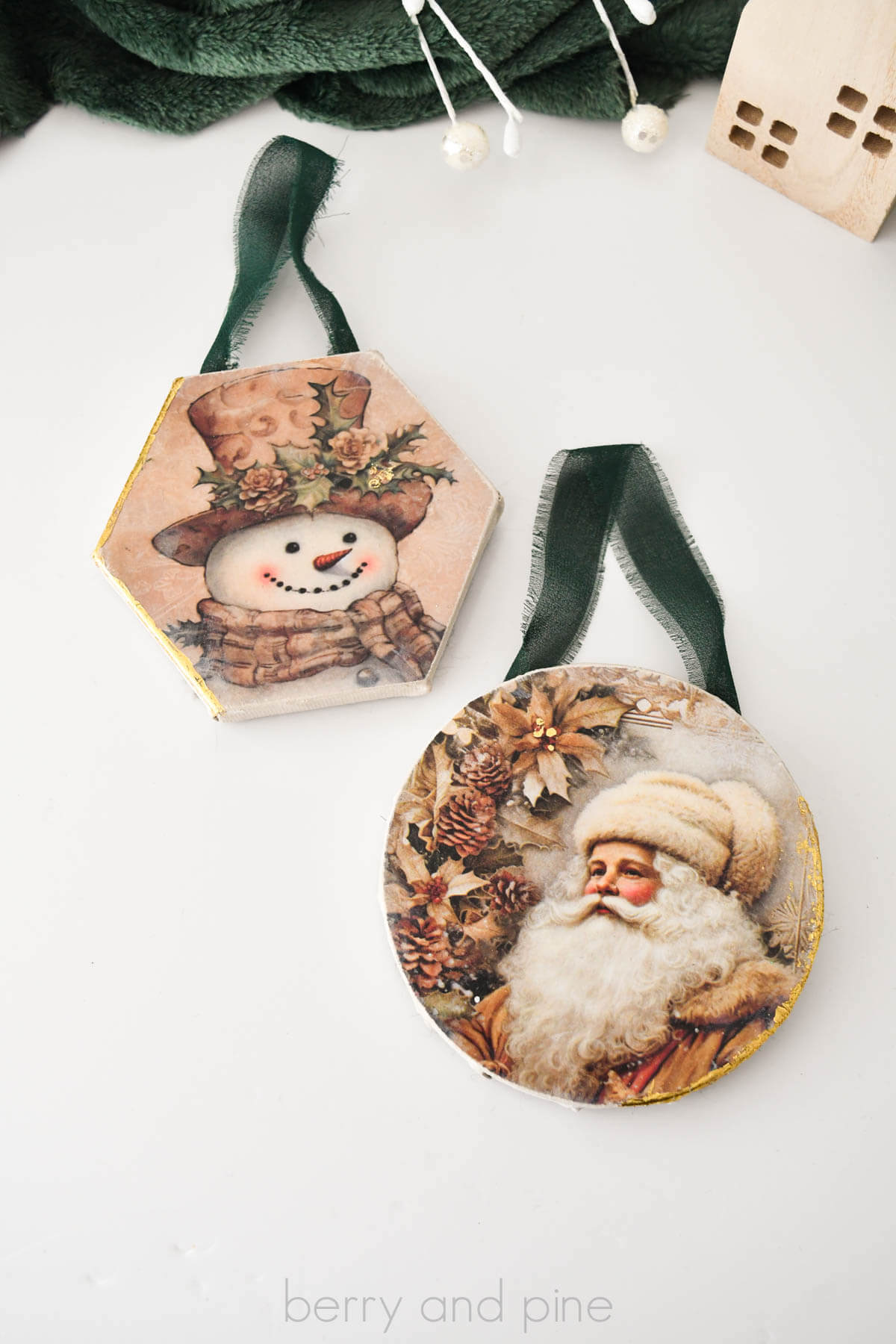 Vertical image of two mini canvas Christmas ornaments made with vintage holiday decoupage papers, chiffon ribbon, and gold foil gilded edges.