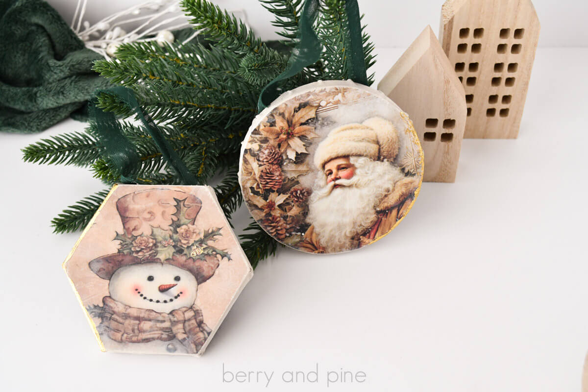 Horizontal image of two mini canvas Christmas ornaments from Dollar Tree made with Santa and snowman vintage papers and gold foil for gilded accents.