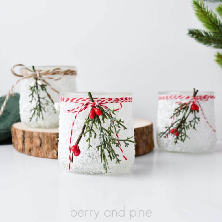 Square image of three recycled glass jars turned into snowy jars with Dollar Tree greenery and berries, tied with twine.