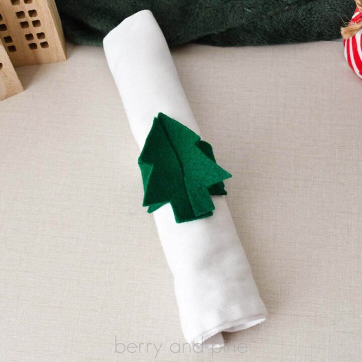 Close up square image of a dark green Christmas tree napkin ring on a white cloth napkin on a linen table.